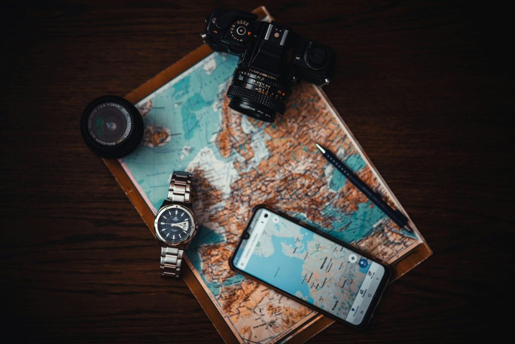 pexels-photo-3243090-3243090 Top view of travel essentials including a map, camera, phone, watch, and lens on a wooden surface.